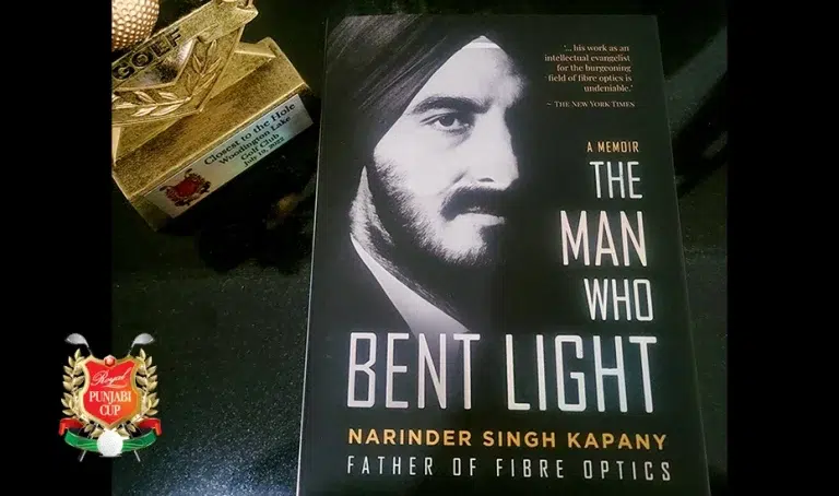 A picture of Narinder S. Kapany's book, "The Man Who Bent Light" atop a black table, commemorating 150 copies donated to Punjabi Golfers Association.
